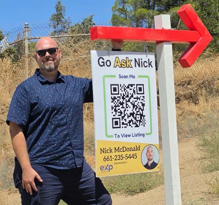 Nick McDonald beside his Go Ask Nick real estate sign and red arrow in the Antelope Valley.